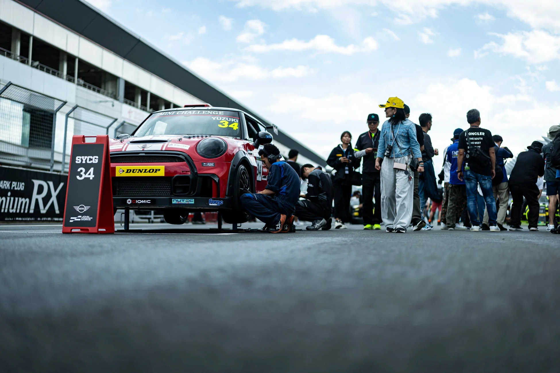 モータースポーツイベントのピットレーンで、赤いMINIレーシングカーがメカニックによって整備されています