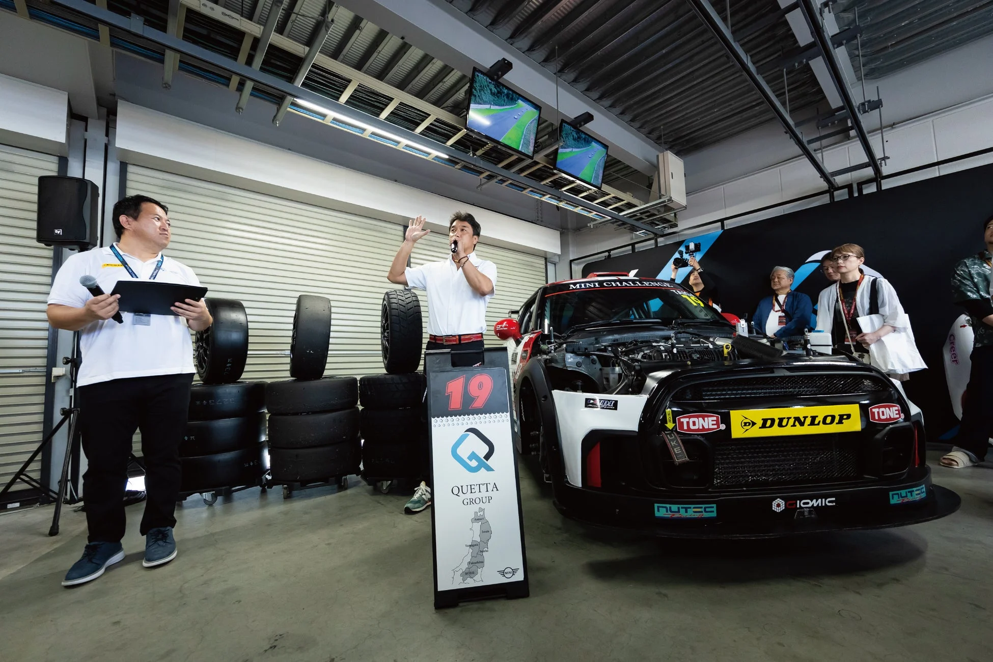 ガレージのような場所で、レースカーを囲んでイベントが開催されています